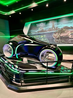 A sleek black concept vehicle with neon blue lighting on display in a futuristic showroom with green ambient lighting.