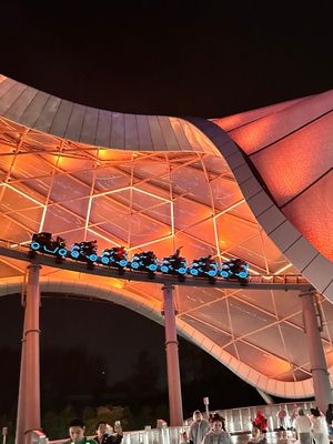 A modern outdoor amphitheater with white curved columns and glowing orange lighting illuminates a performance at dusk.