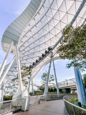 Modern walkway with geometric white canopy structure and curved glass panels creates an elegant architectural perspective.