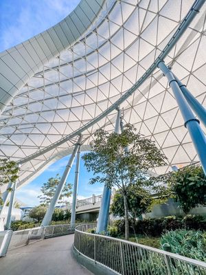 Modern architectural walkway with curved glass roof, metal support beams and tropical landscaping at Marina Bay Sands Singapore.
