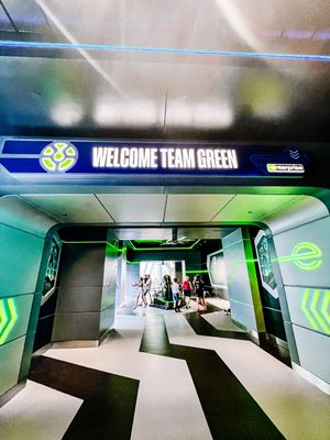 Sleek futuristic sports facility entrance with green lighting and 'Welcome Team Green' signage on blue display panel.