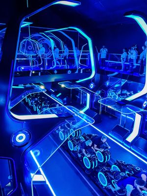 Futuristic blue-lit interior of a theme park ride with glowing neon accents and curved walls creating an immersive space.