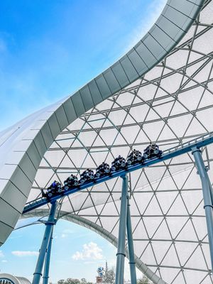 Rollercoaster track curves against a geometric white domed structure and blue sky at Ferrari World Abu Dhabi.