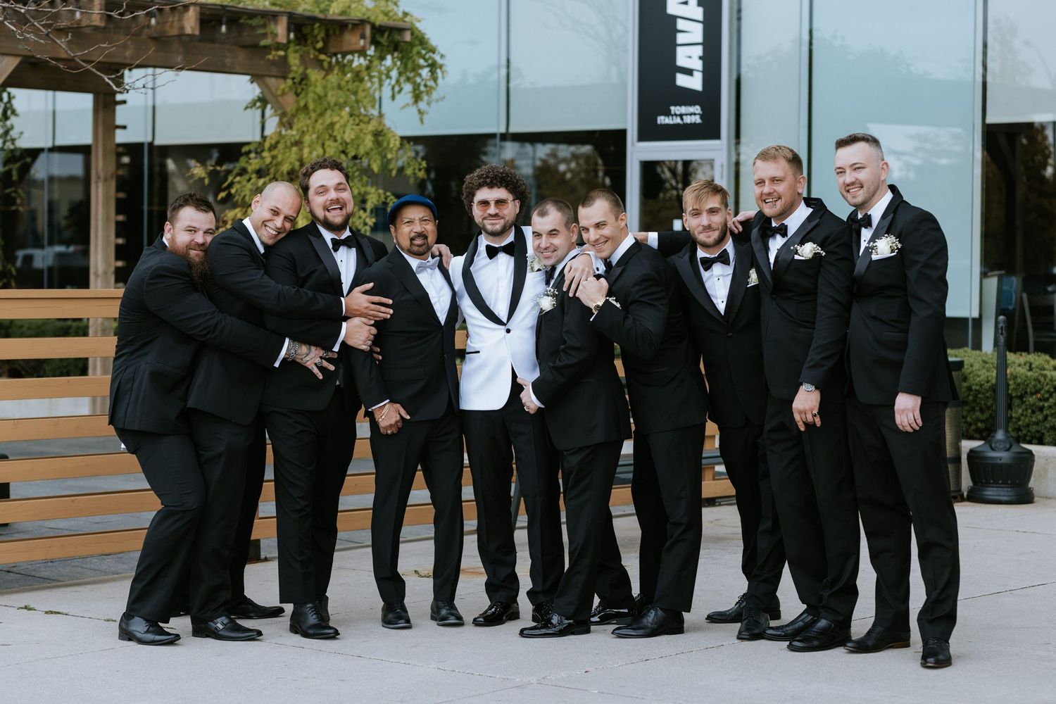 Groomsmen in formal attire share a candid moment together outside during wedding celebrations.
