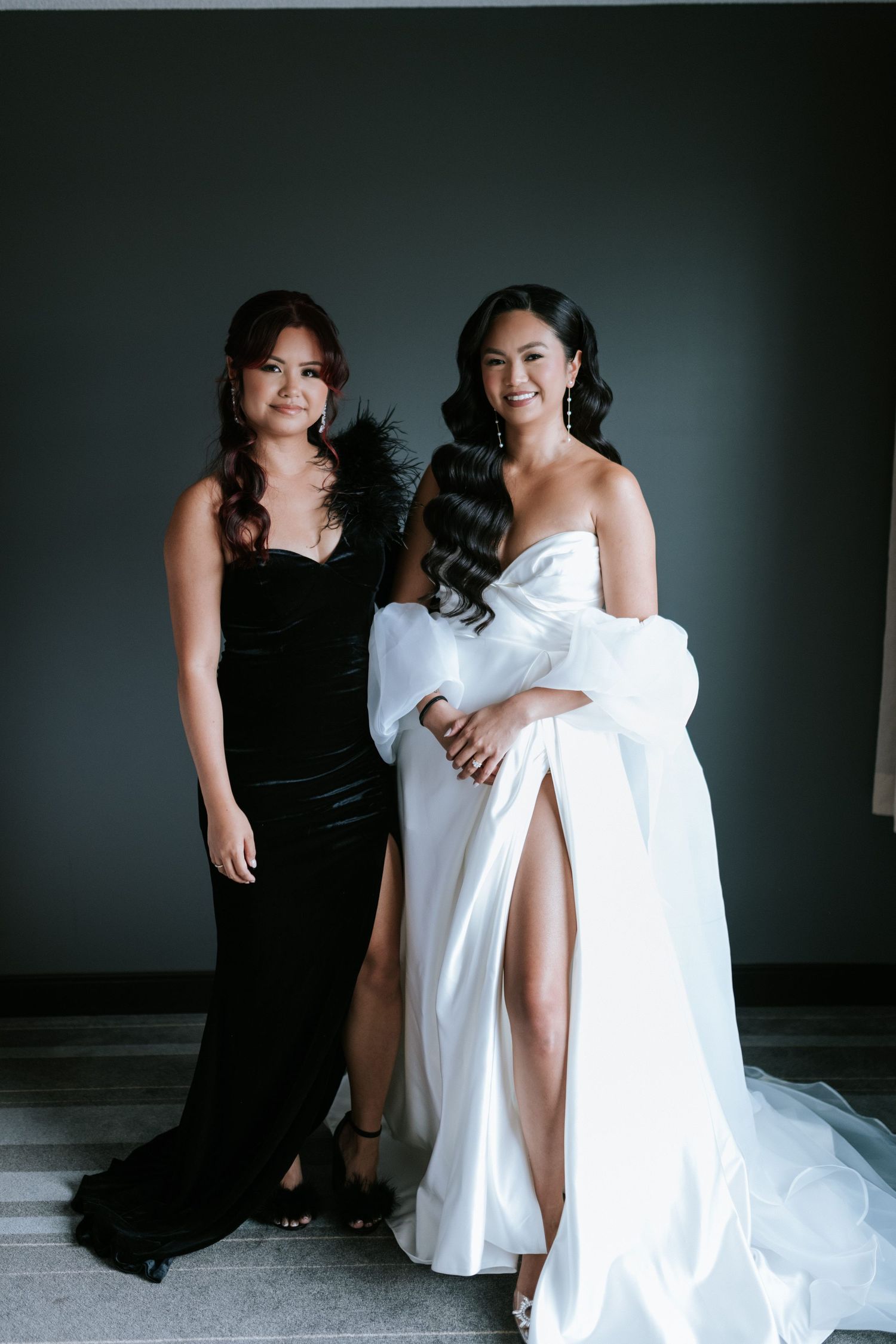 Two women pose together in black and white formal dresses against a dark grey backdrop.