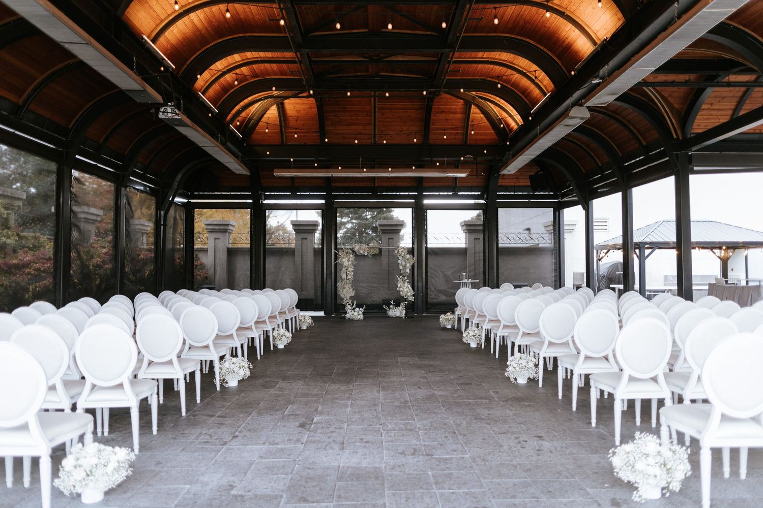 Wedding ceremony venue with rows of white chairs under a vaulted ceiling with warm lighting.