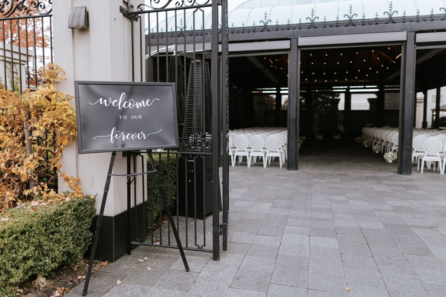 Welcome sign stands at entrance gate to outdoor wedding venue with modern industrial design.