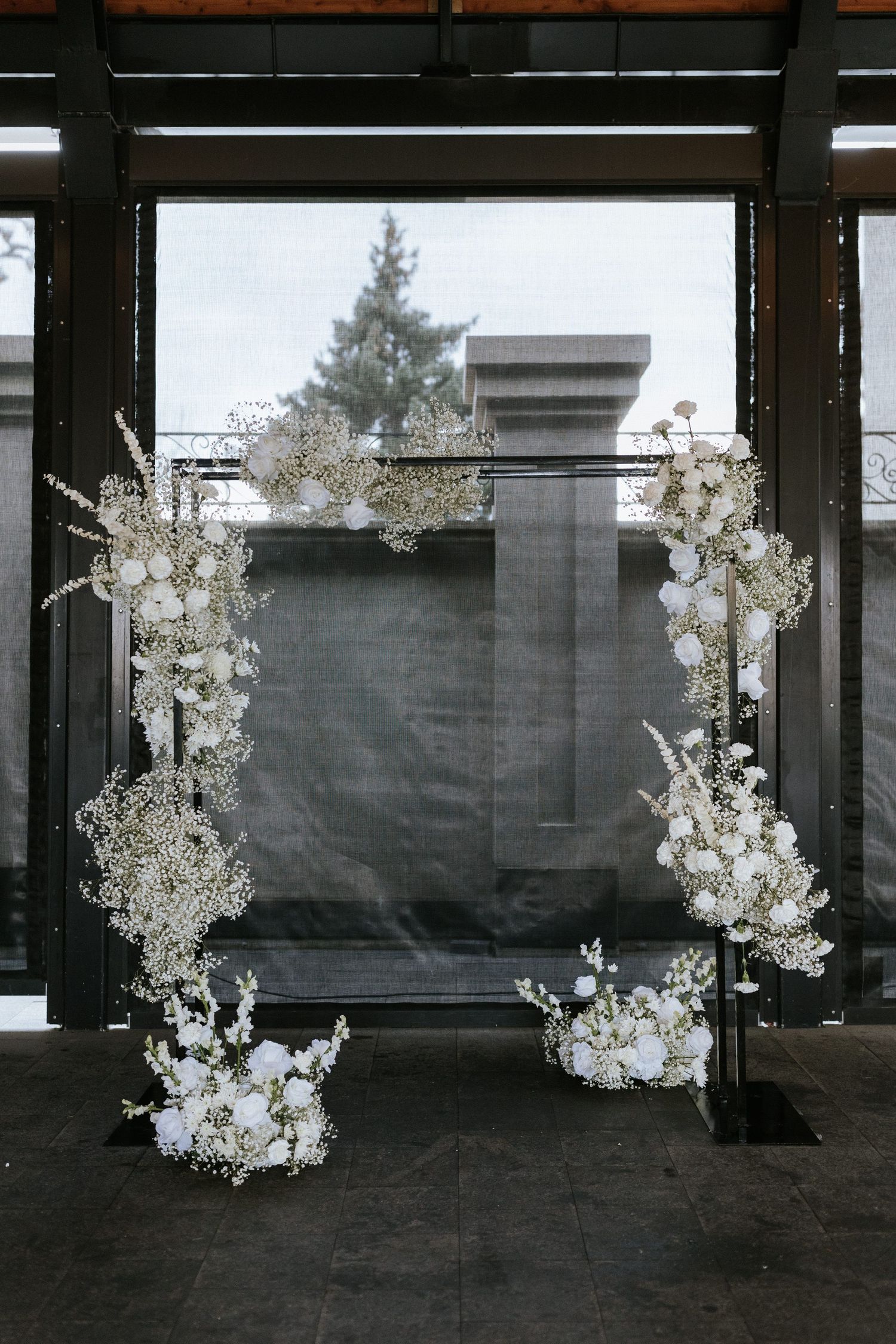 A white floral wedding arch with delicate baby's breath and blooms creates an ethereal ceremony backdrop.