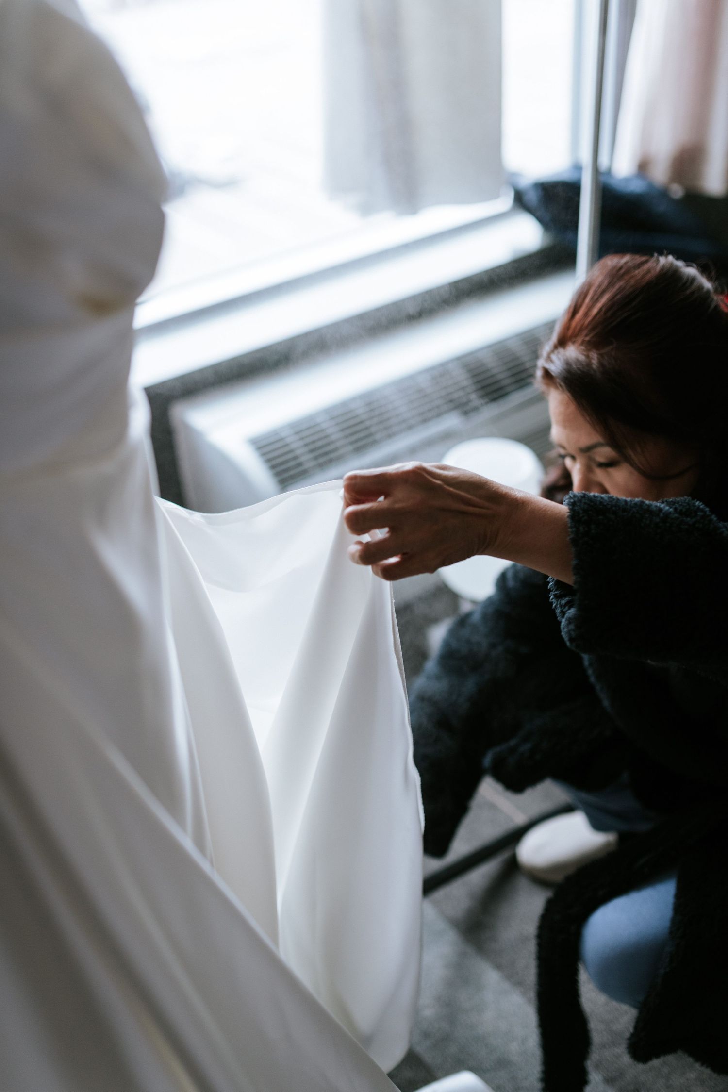 Hands carefully adjusting white fabric in front of a window.