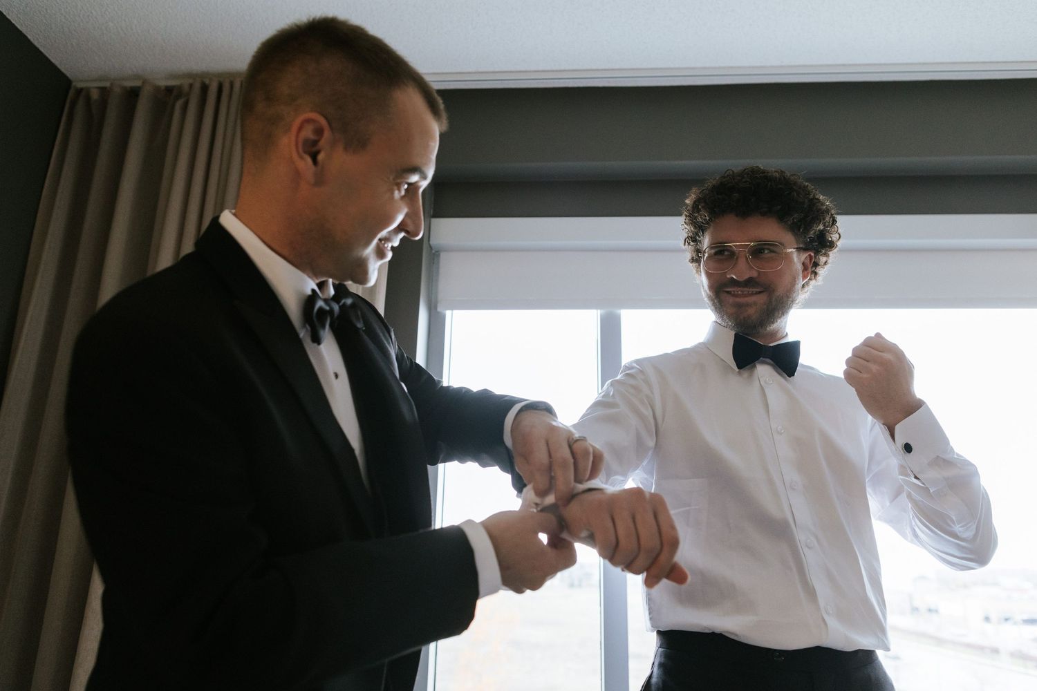 Two people in formal attire helping each other prepare bow ties.