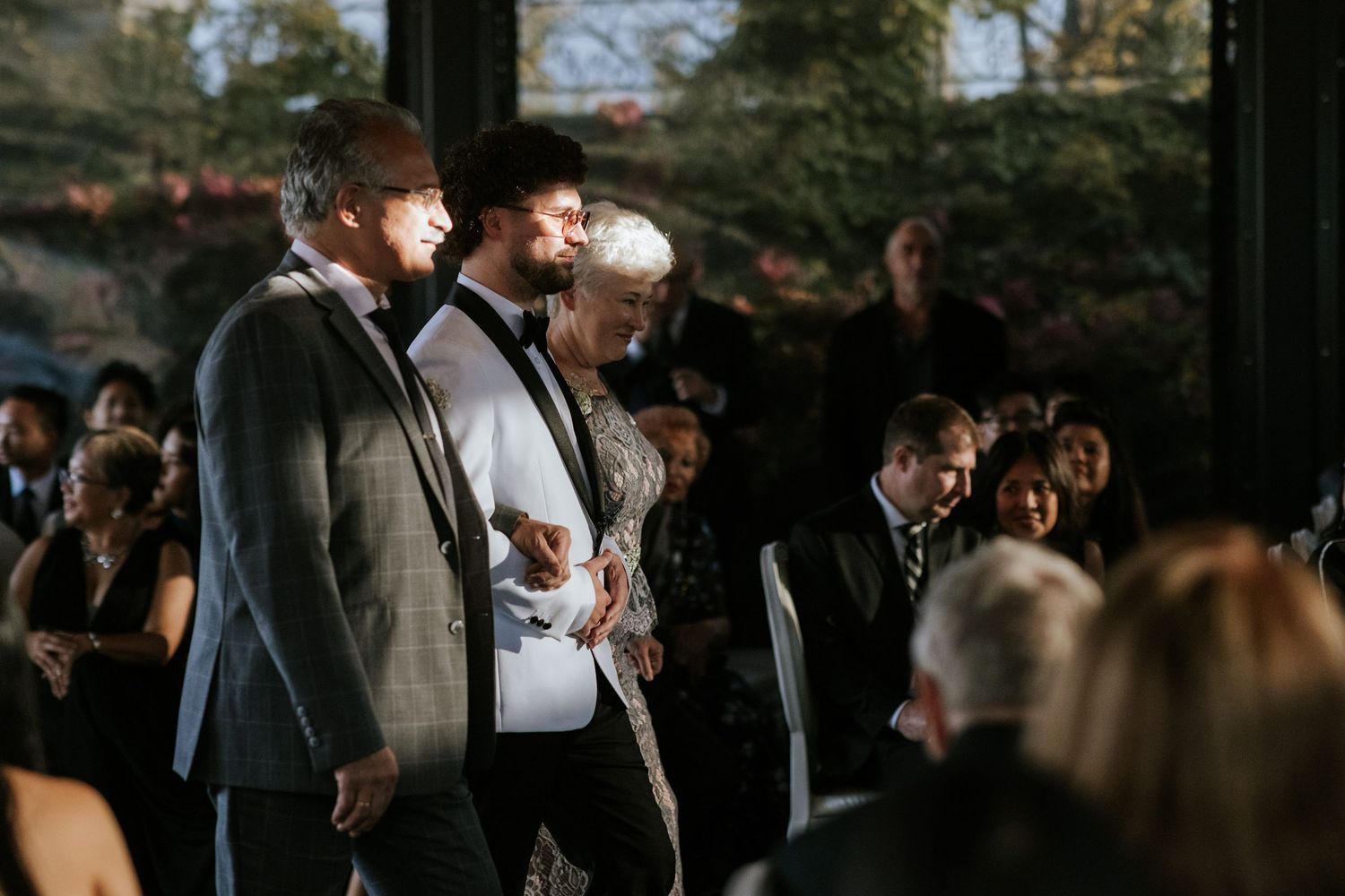 Wedding ceremony attendees stand during an emotional moment in a modern indoor venue.