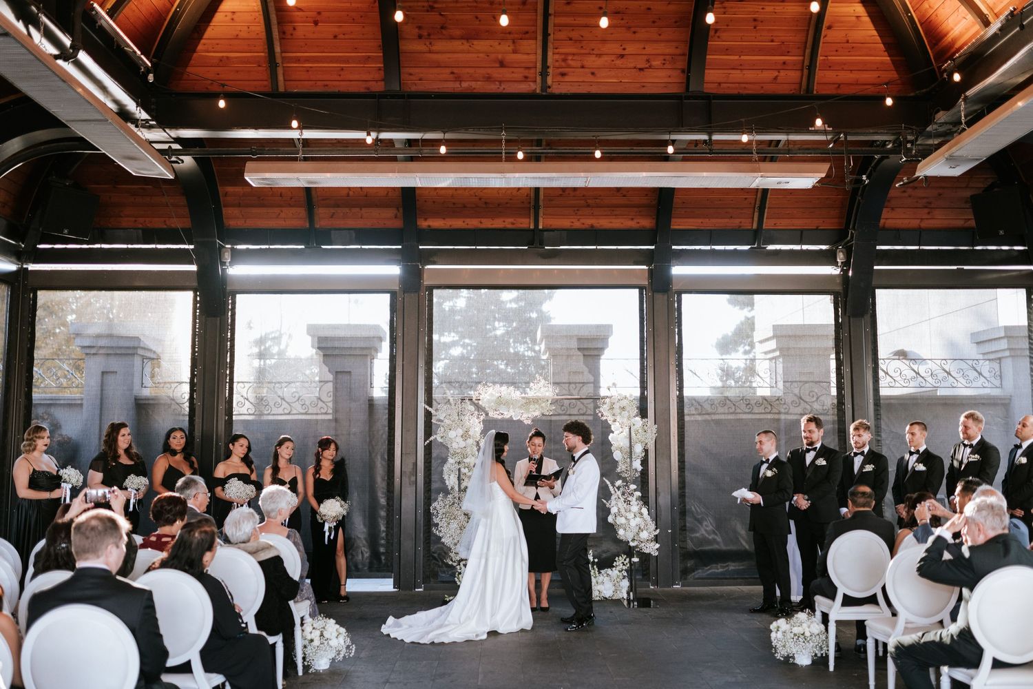 An indoor wedding ceremony with floor-to-ceiling windows overlooking a cityscape.