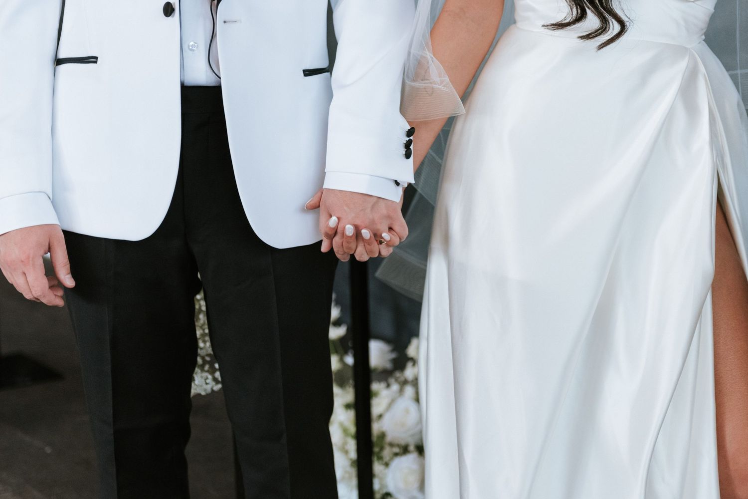 A close-up of a couple's formal wedding attire showing a white tuxedo jacket and bridal gown.