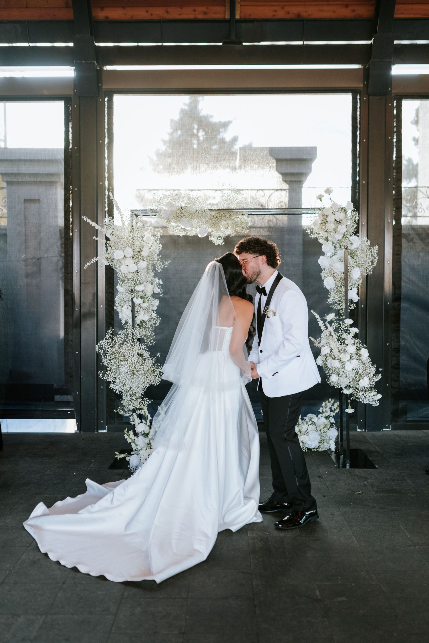 A romantic wedding moment with white floral arrangements framing a couple under an arched structure.