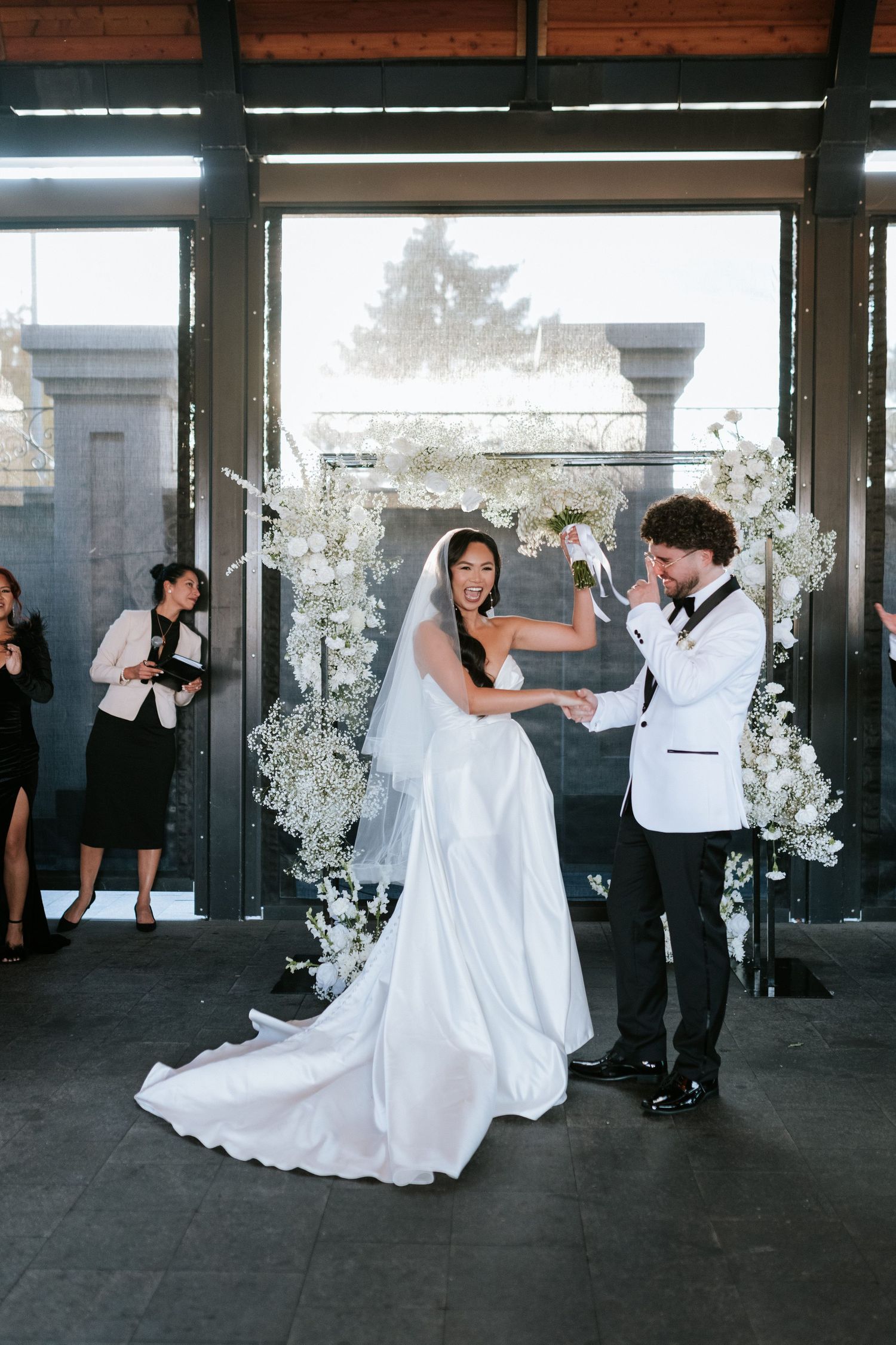 Wedding celebration in modern venue with floor to ceiling windows and white floral arch.