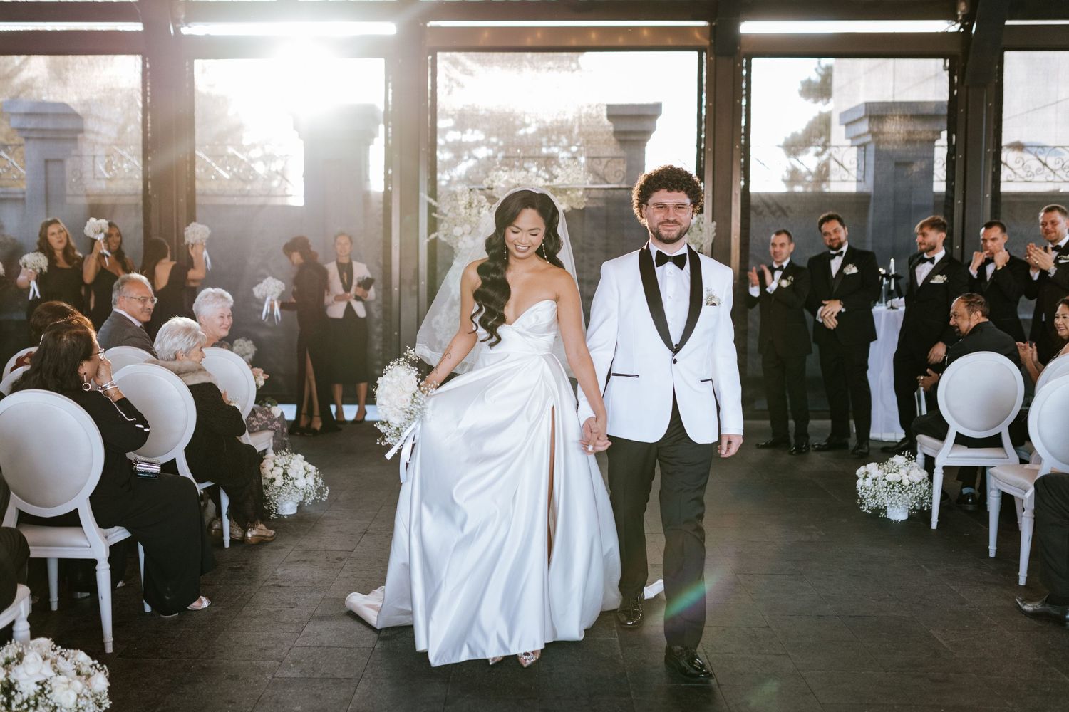 Wedding ceremony exit with guests clapping in modern venue with large windows.