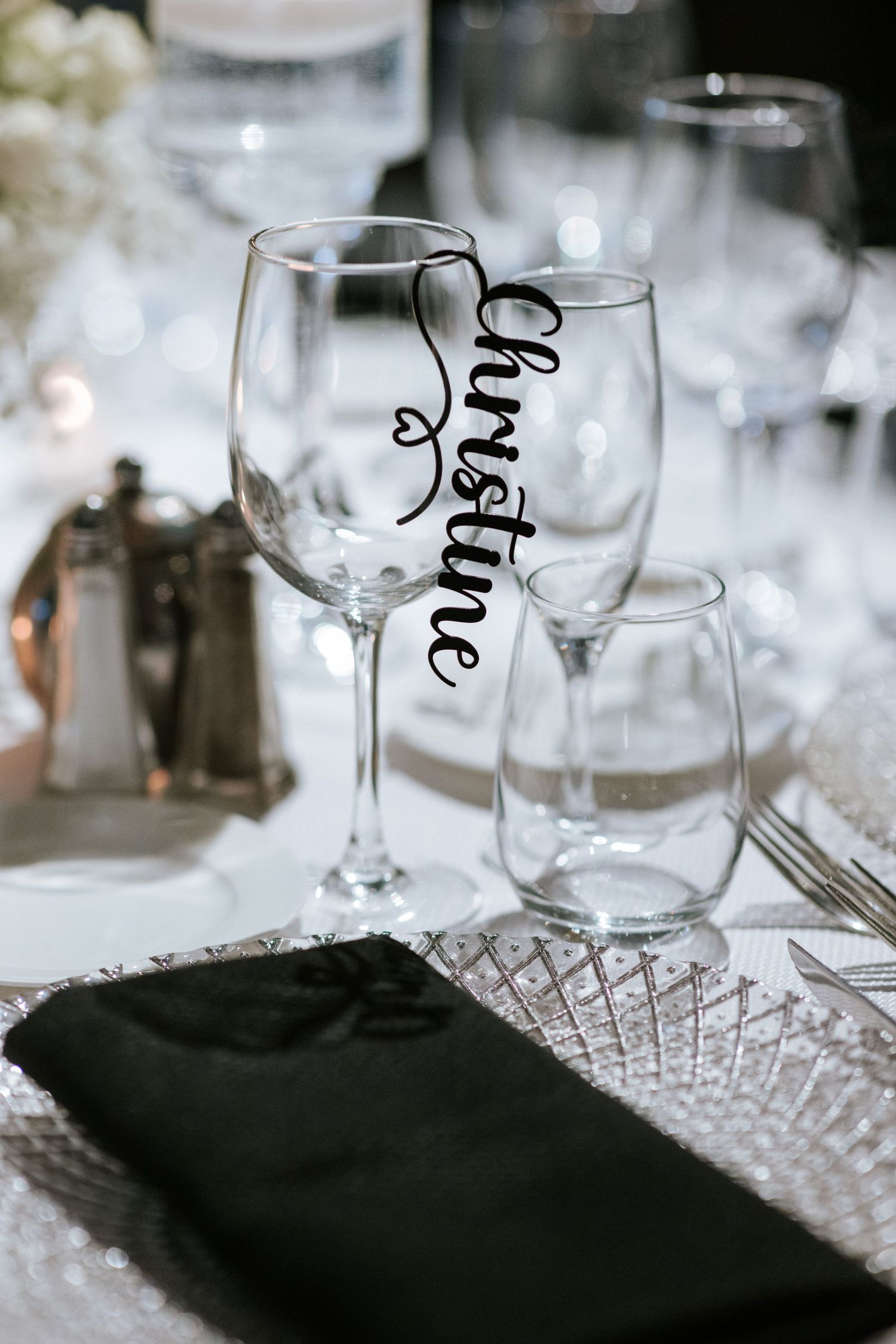 Wedding reception place setting with personalized wine glass and black napkin.