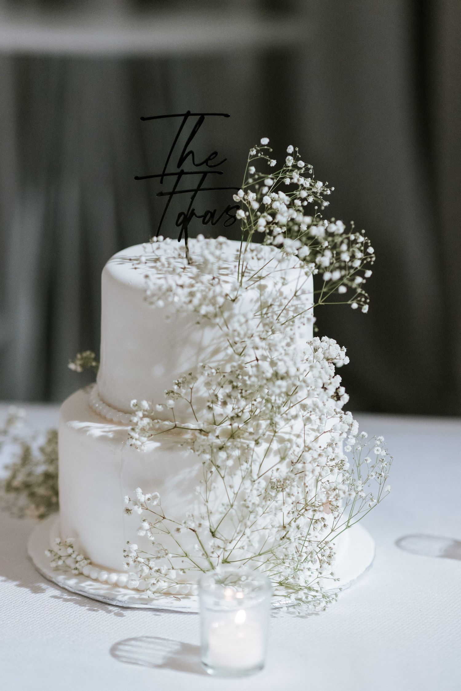 Two-tier white wedding cake decorated with baby's breath flowers and modern black cake topper.