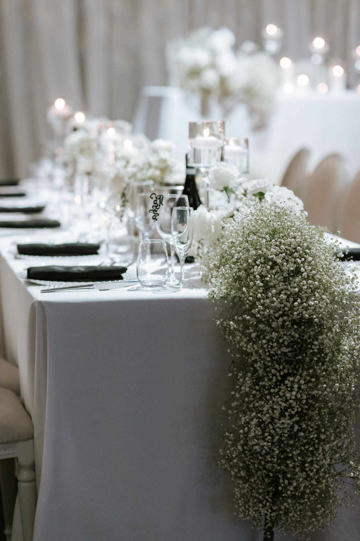 Elegant white wedding table setting with baby's breath flowers and candle centerpieces.