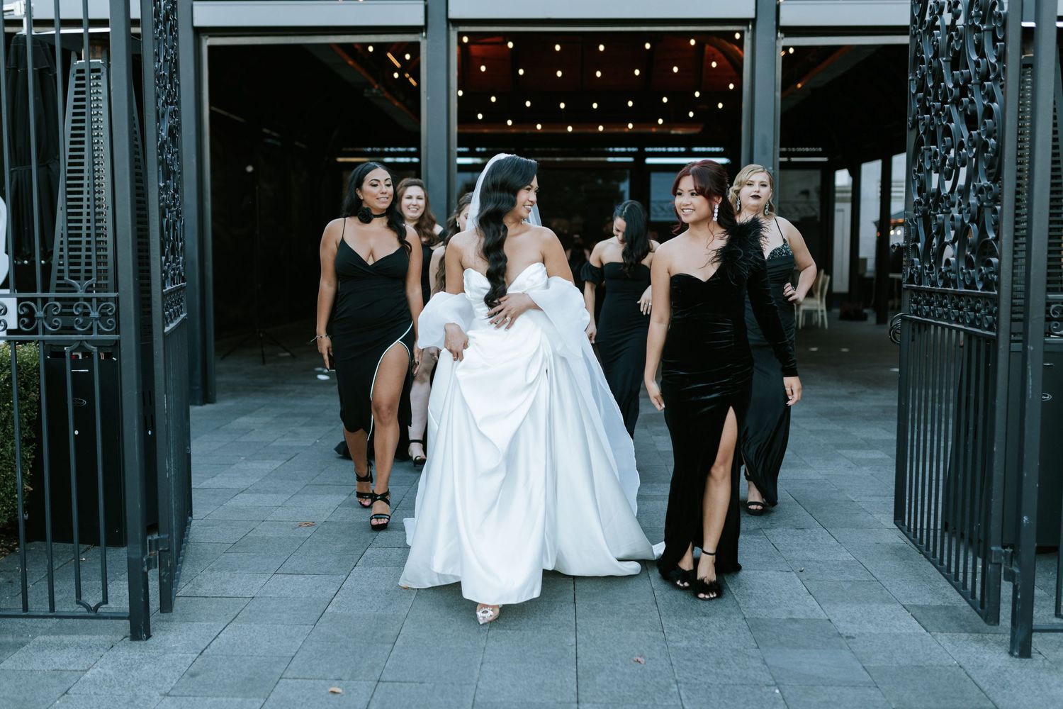 Elegant wedding party walking through ornate gates in black and white formal attire.