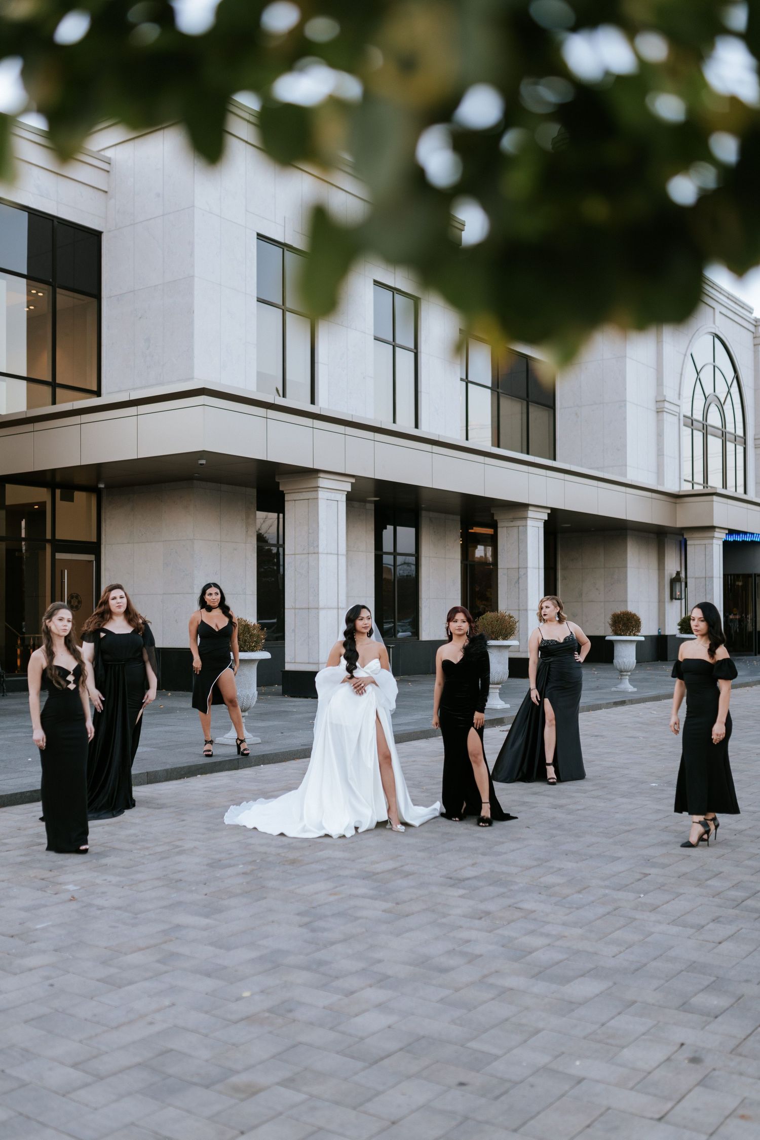Wedding party posed outside modern white building with bride in center wearing flowing gown.