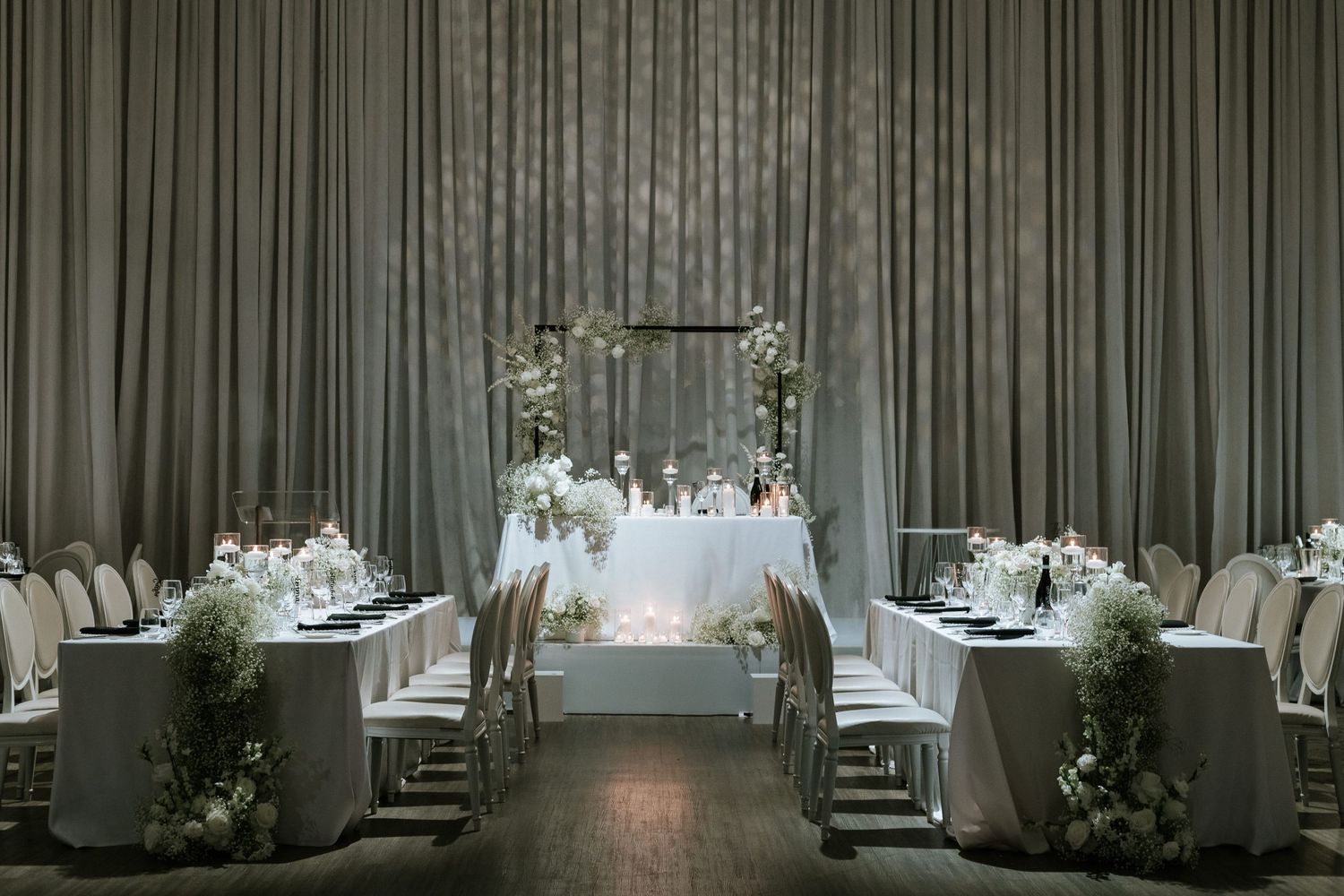 Modern wedding reception setup with draped grey backdrop and white floral arch.