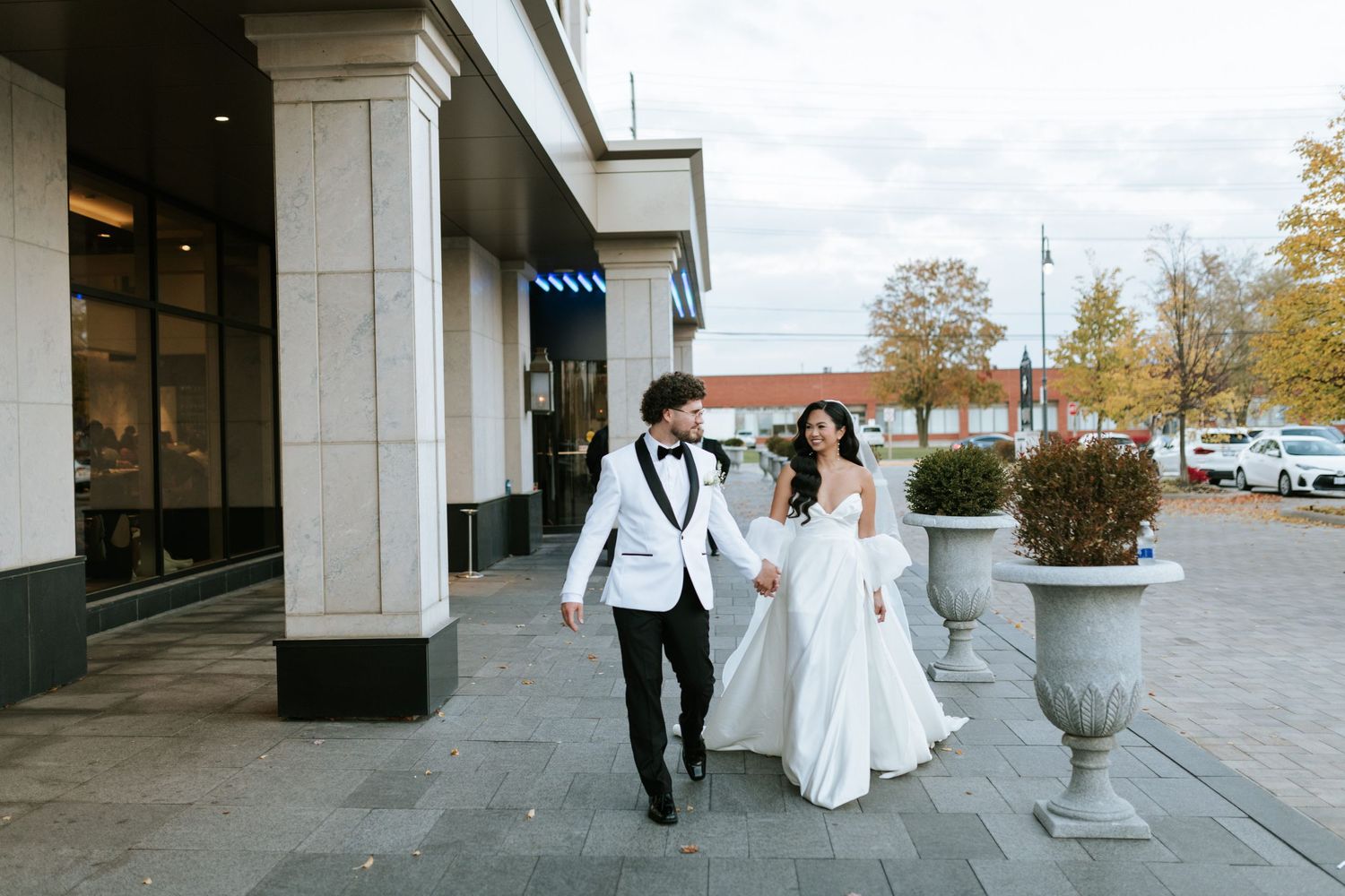 Elegant couple walking together outside modern building during wedding day.