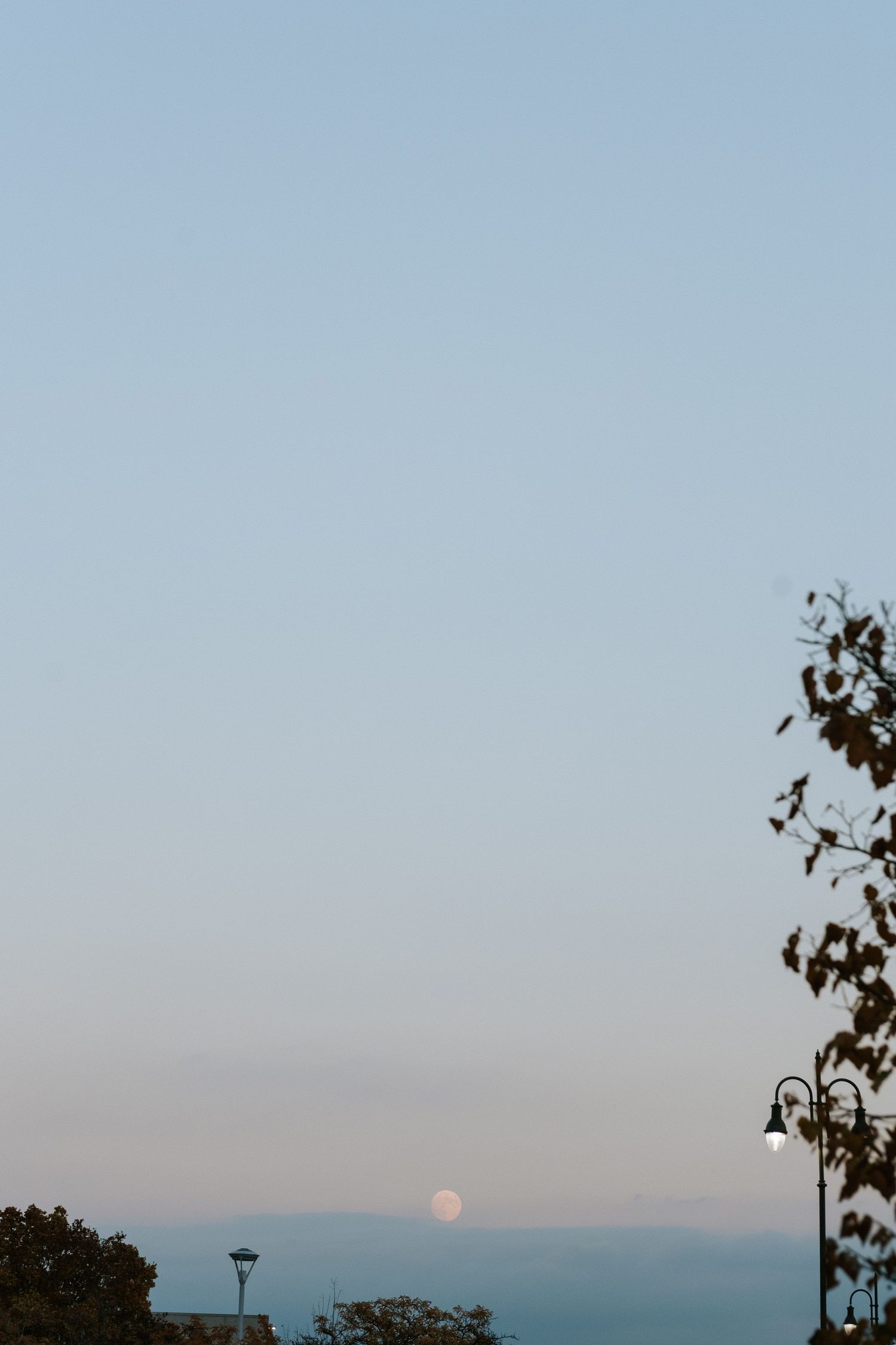 Serene dusk sky with full moon rising above distant mountains.