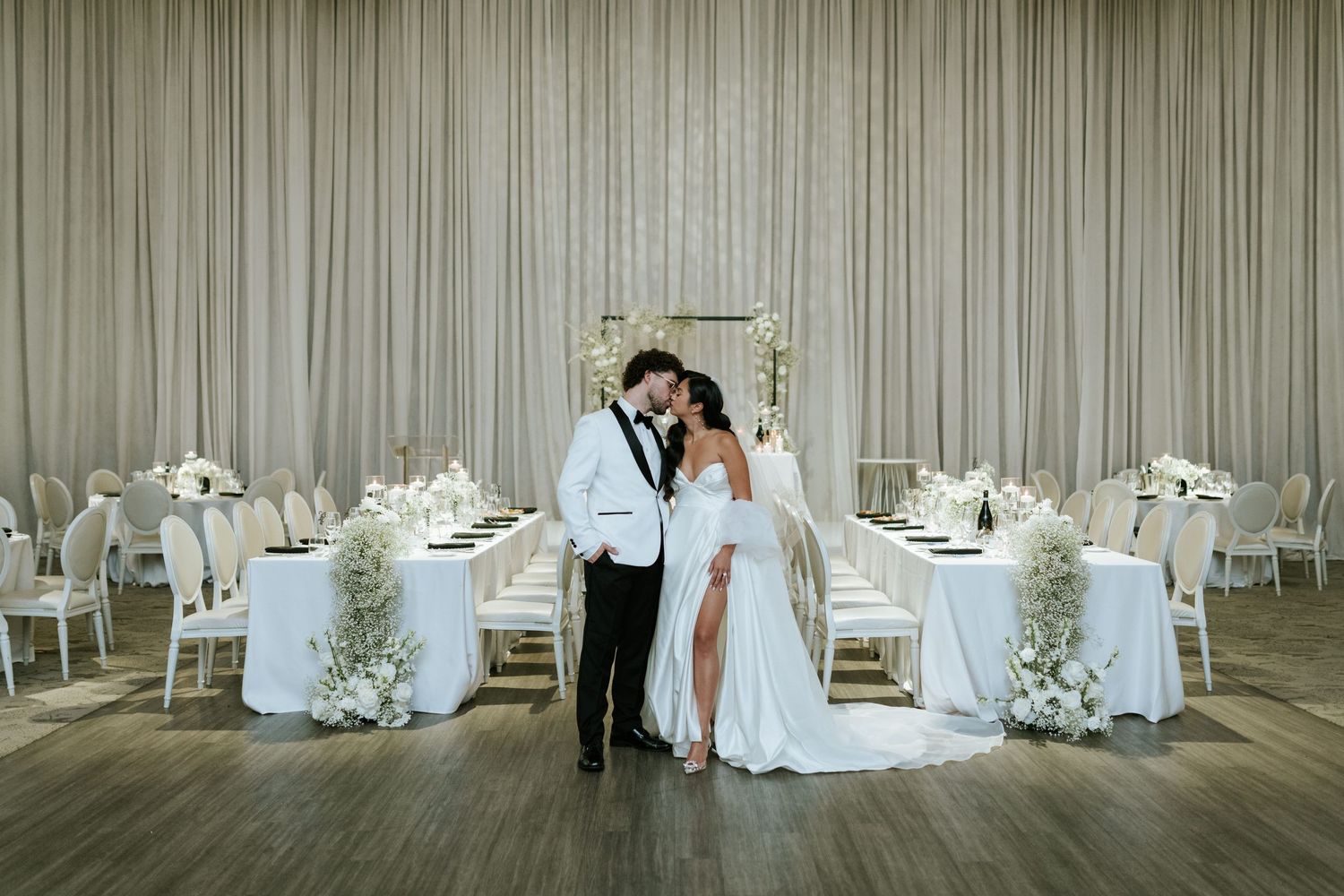 Elegant wedding reception venue with white decor and dramatic curtained backdrop.