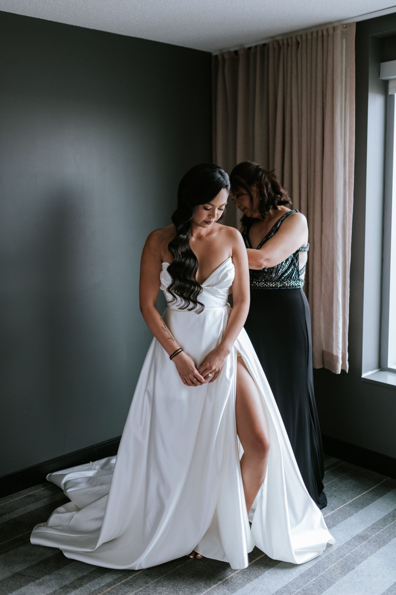 Final adjustments being made to an elegant white wedding gown in a modern room.