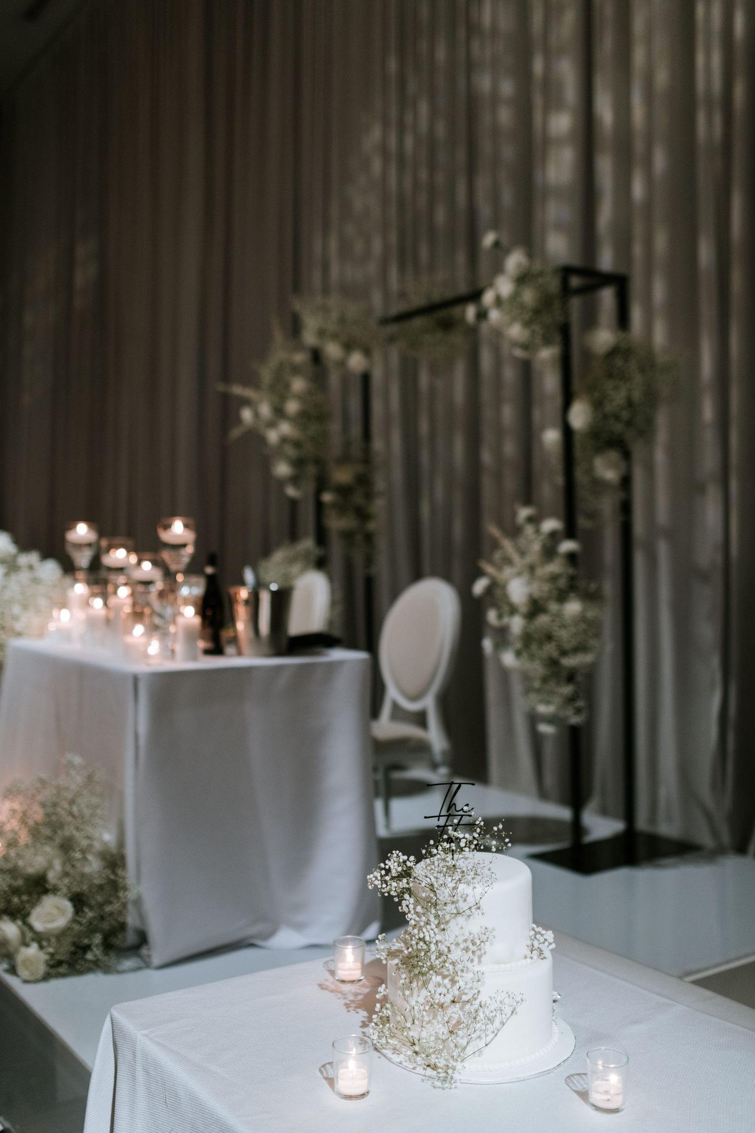 White wedding cake decorated with baby's breath sits on table with candles and floral arrangements.