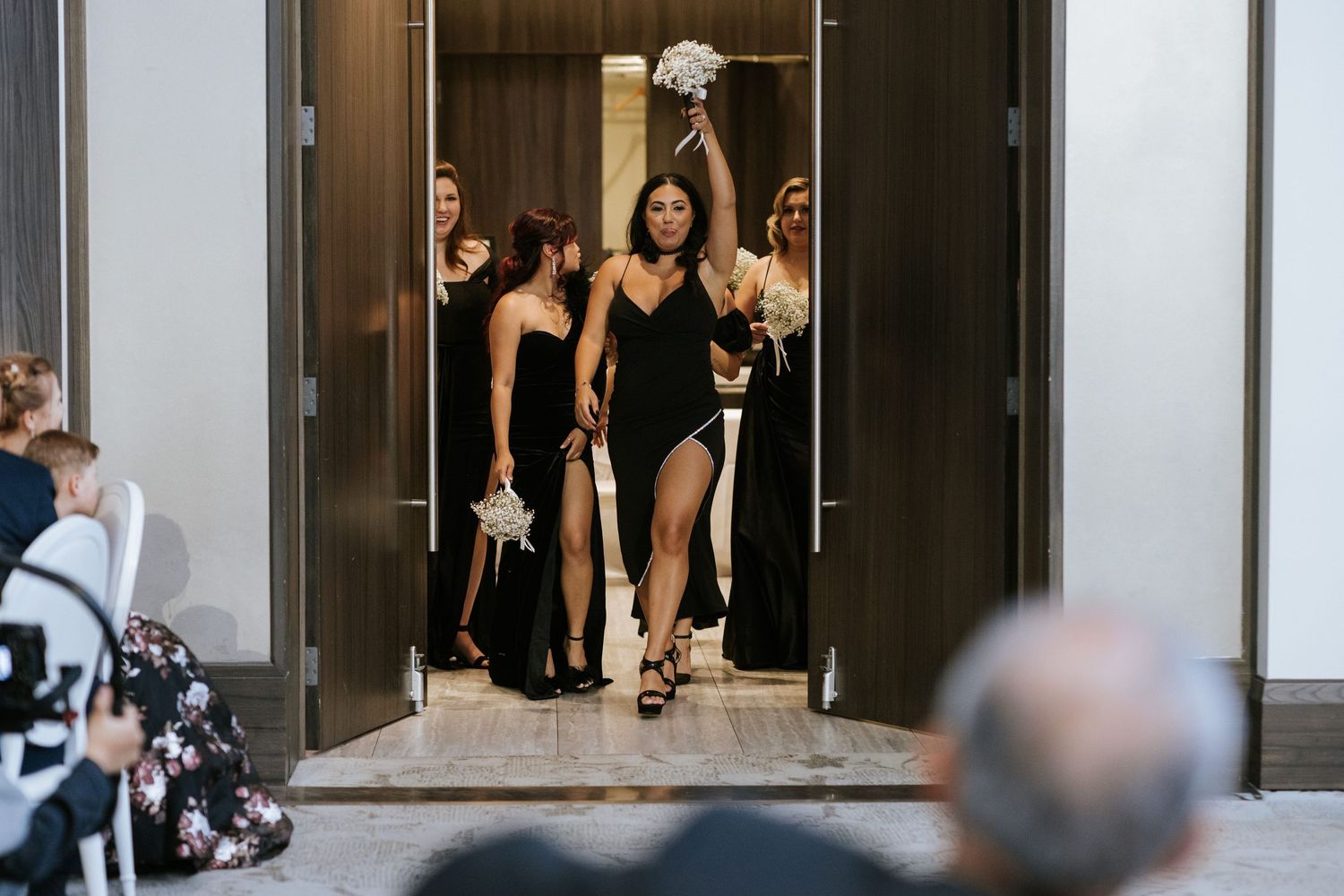 Group in formal black dresses making dramatic entrance through doorway.