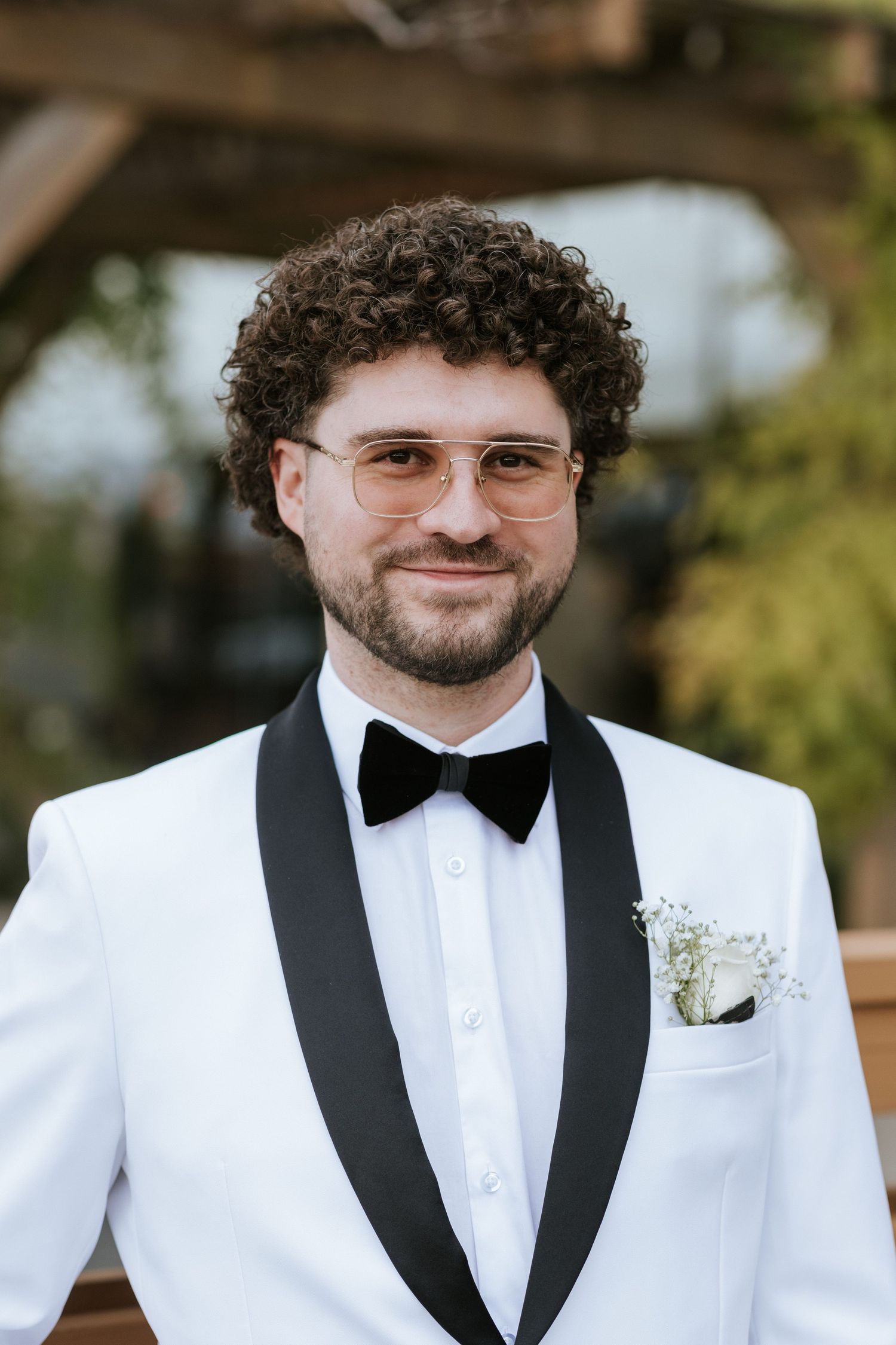 A person wearing a white tuxedo jacket with black lapels and bowtie smiles at the camera.