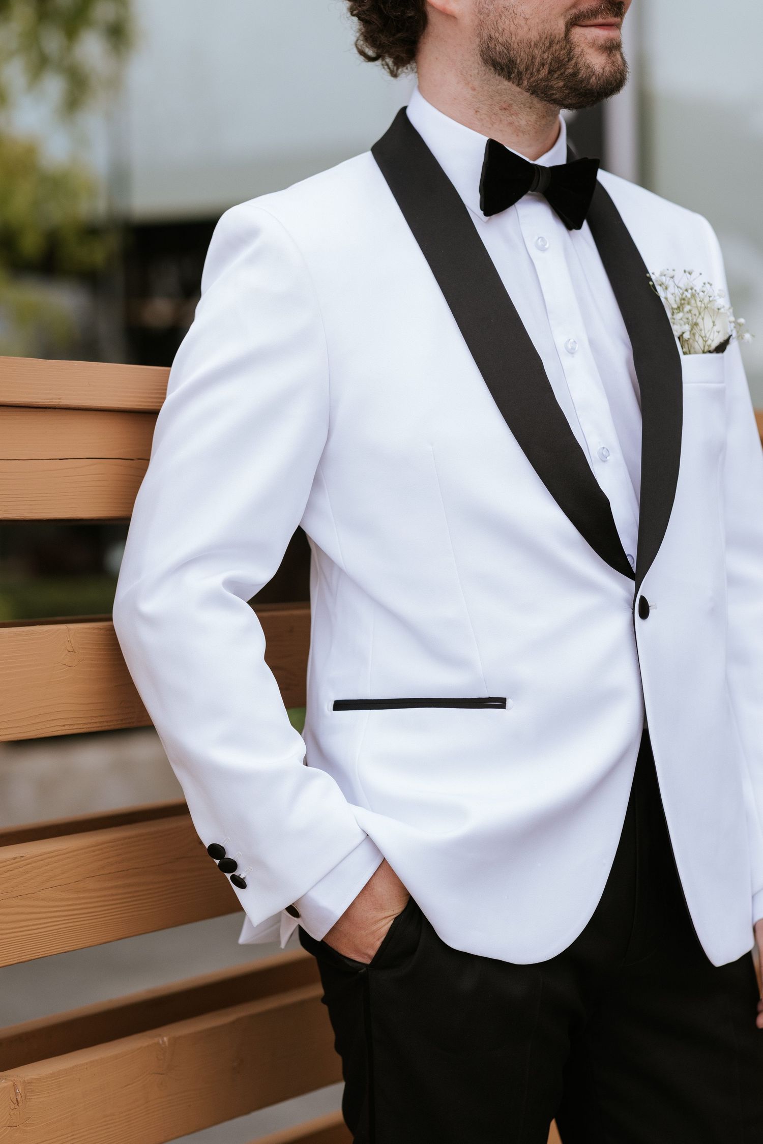 A detailed view of a white tuxedo jacket with black shawl lapel and boutonniere.