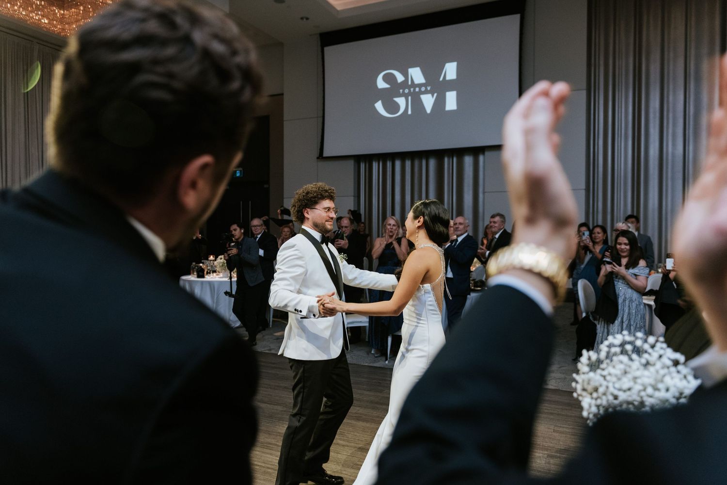 Wedding couple dancing while guests raise their hands in celebration.