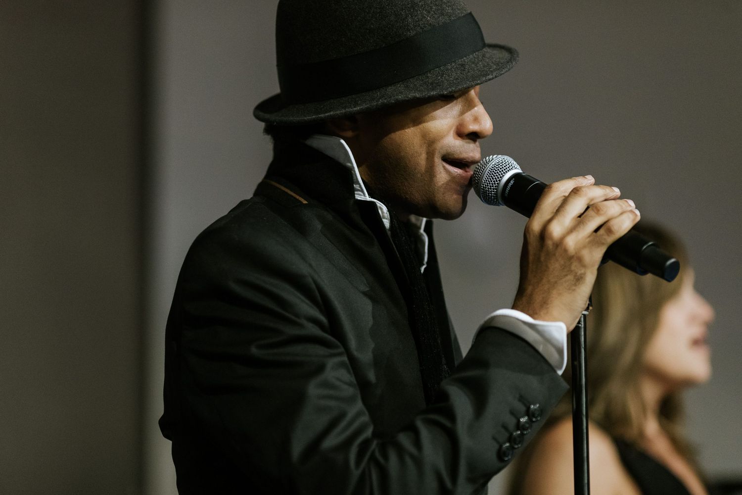 Entertainment performer in black suit and fedora singing into microphone.