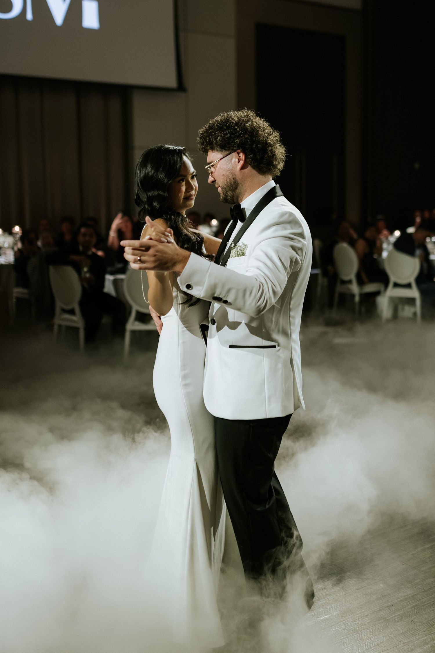 Newlyweds share their first dance surrounded by atmospheric fog effects on their wedding dance floor.