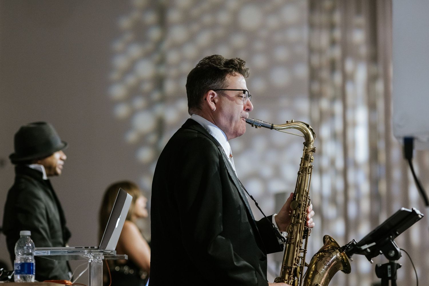 Saxophone player performs at elegant wedding reception with sparkle effects in background.
