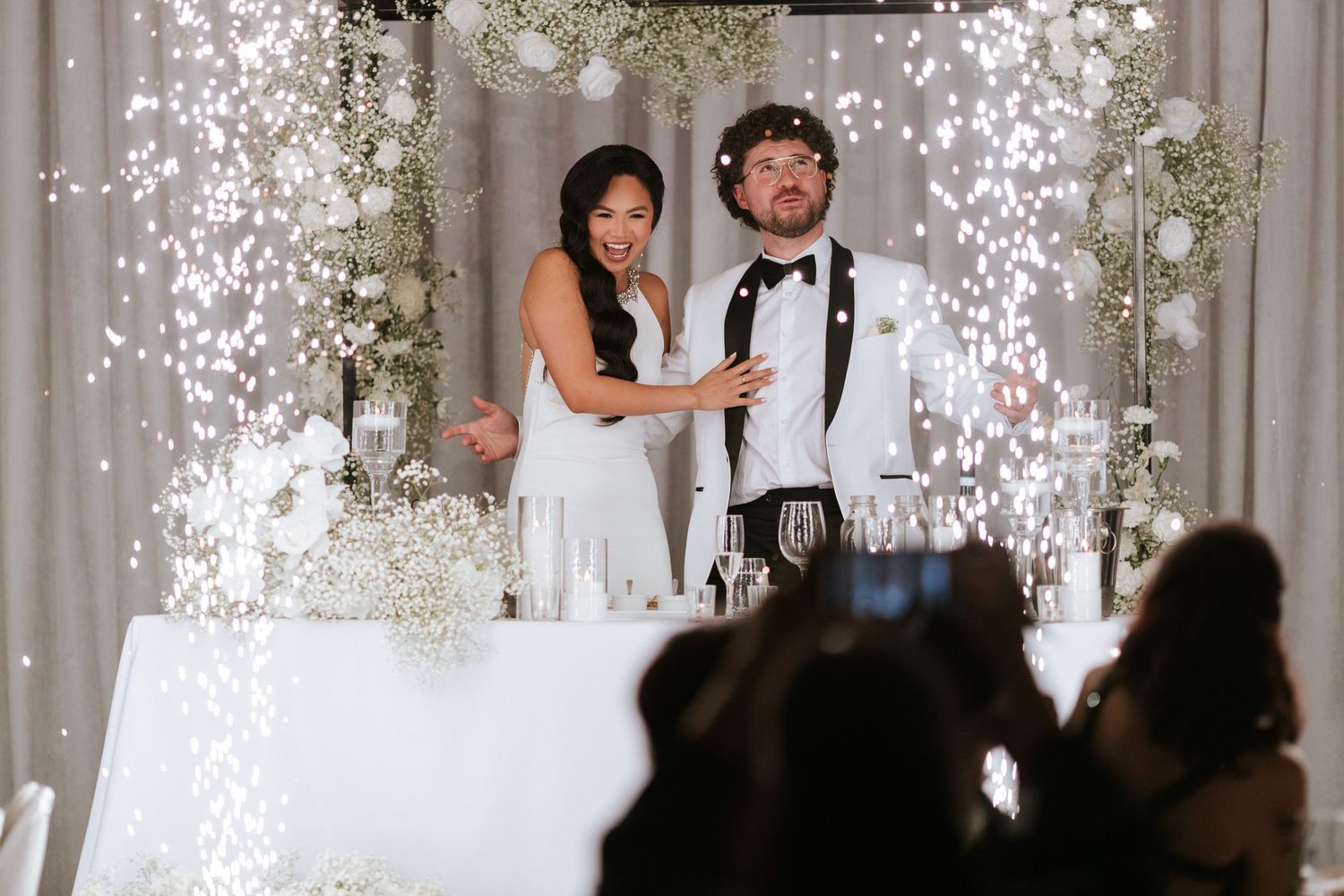 Couple stands at elevated head table with sparkler effects during wedding reception toasts.