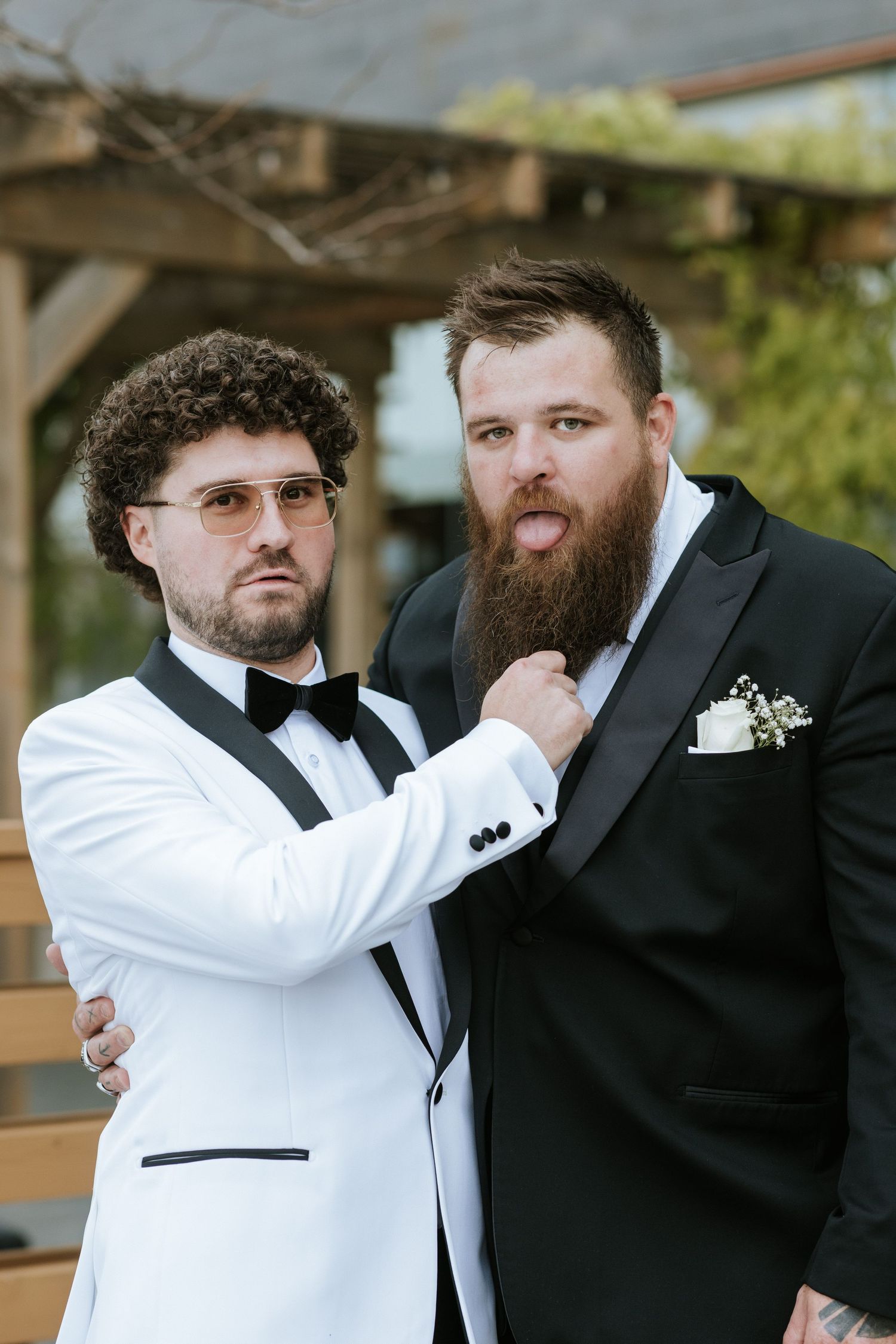 Two people in contrasting black and white tuxedos pose together outdoors.