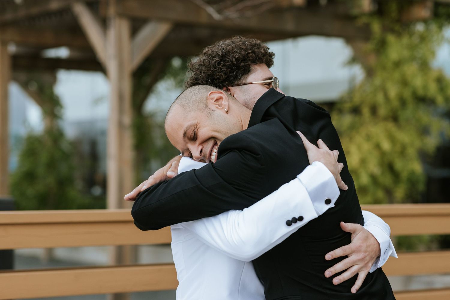 Two people share an emotional embrace on a wooden deck during a formal event.