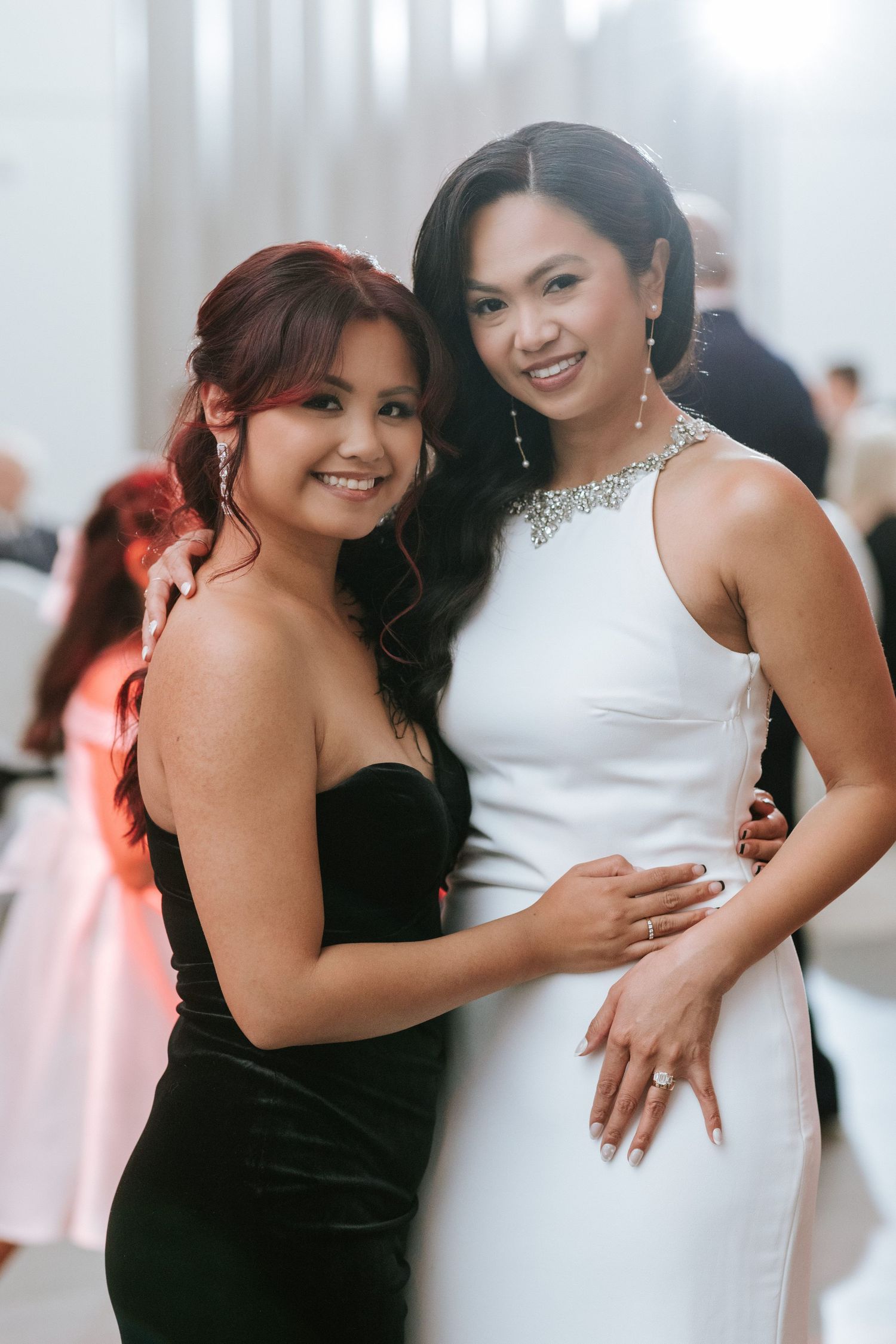 Two wedding guests pose together at reception, one wearing black and one in white formal attire.