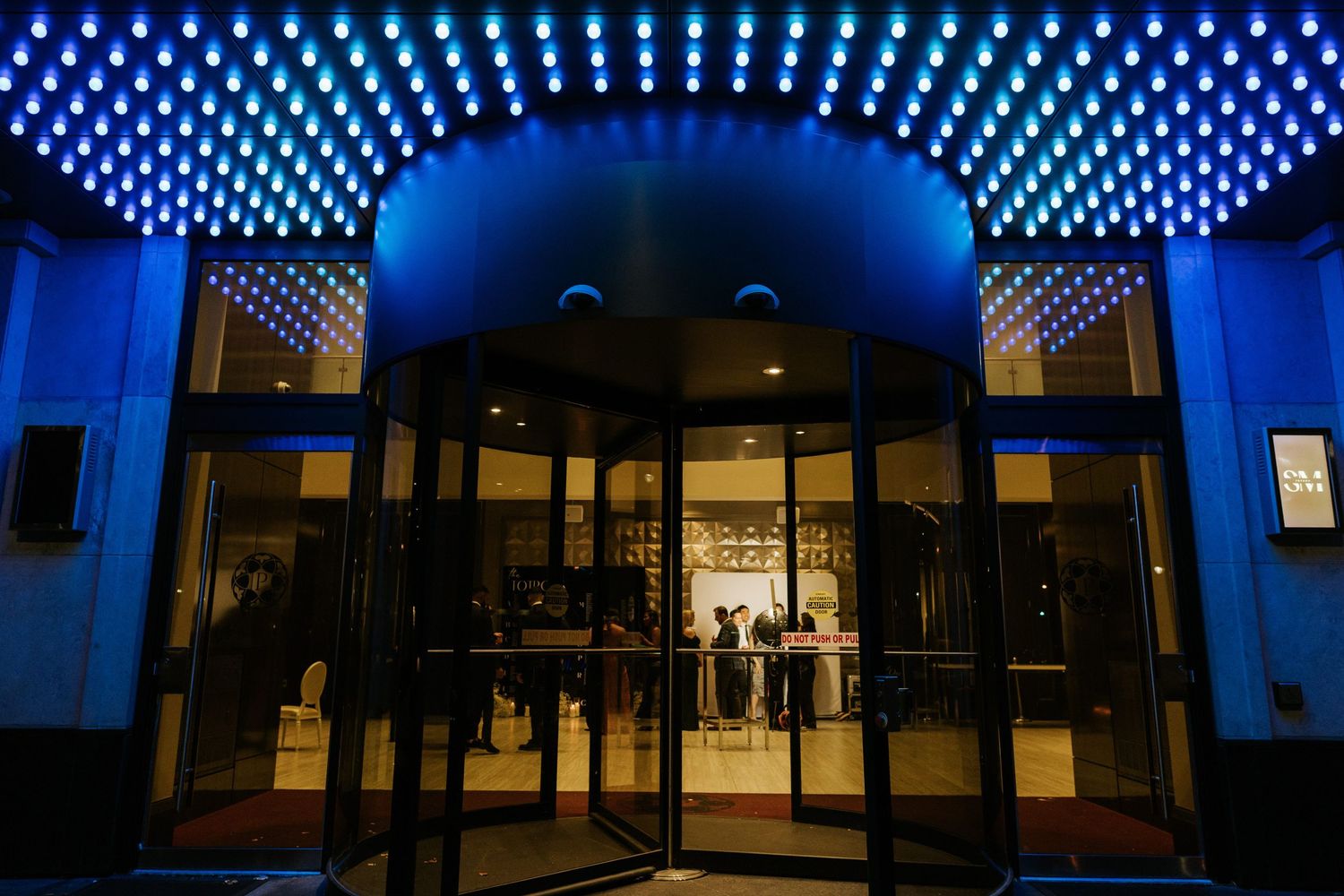 Modern building entrance with illuminated blue LED lights creating a dramatic geometric pattern on the ceiling.