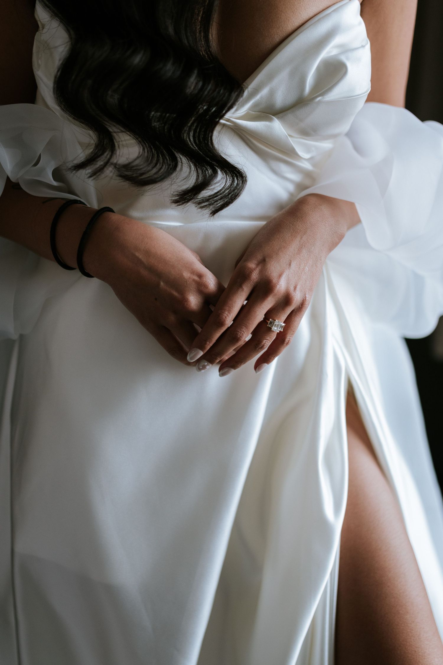 Close-up shot of hands folded over a white wedding dress with delicate details and flowing fabric.