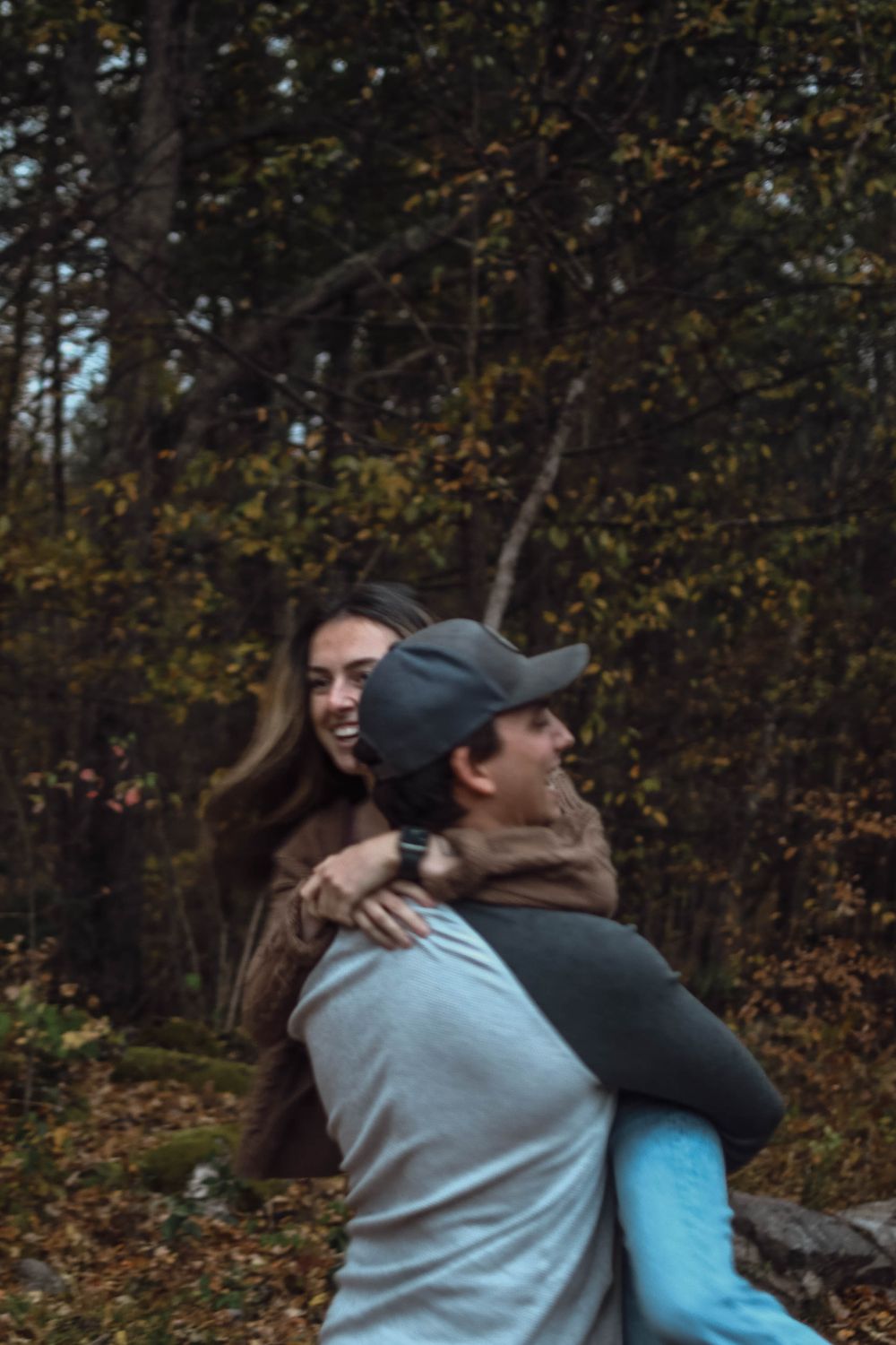 A couple shares a playful moment embracing outdoors in an autumn forest setting during golden hour.