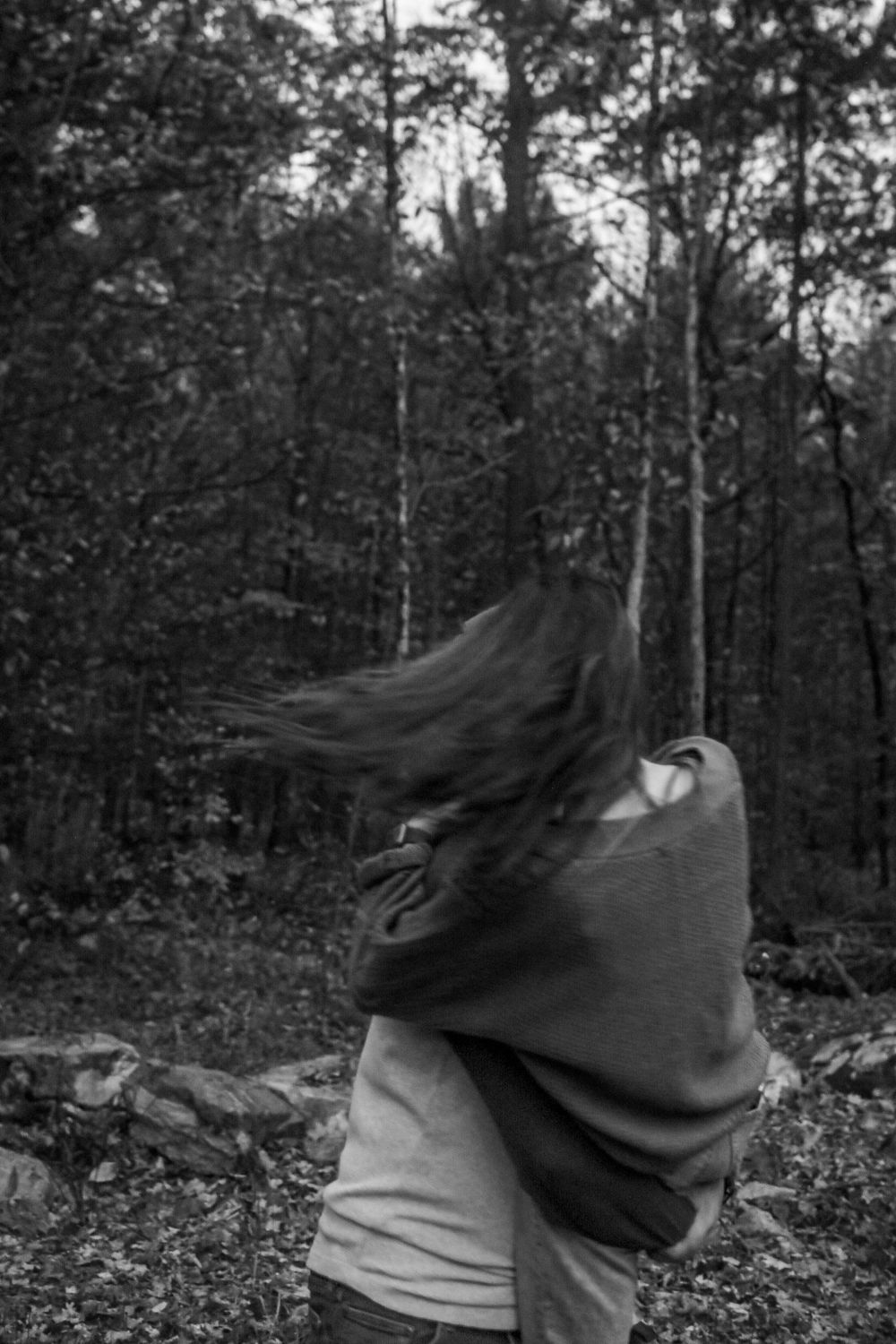 Black and white photo of a person with long windswept hair in a forest setting, creating a dynamic motion effect.