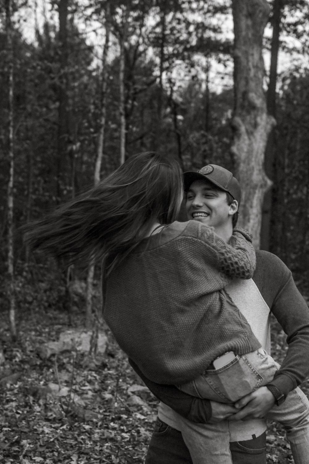 A romantic black and white moment captured in the woods as a couple embraces and shares a joyful laugh together.