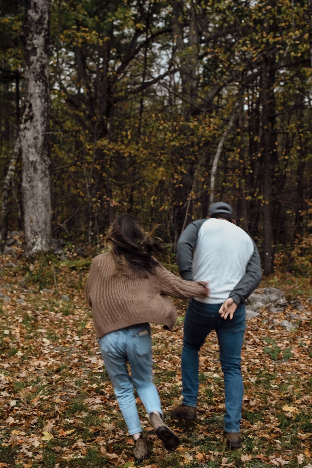 Two people walk together through a forest path covered in fallen autumn leaves on a crisp fall day.