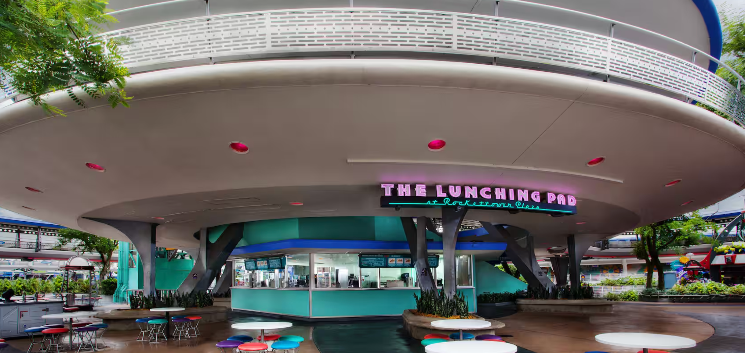 Retro-style teal and white luncheonette counter with curved overhang and classic diner signage at a theme park.
