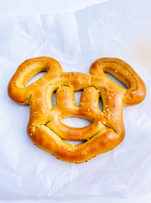 A golden-brown Mickey Mouse shaped pretzel with salt crystals on white parchment paper.